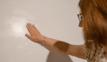 Een bezoeker voelt met de platte hand aan een van de schilderijen.