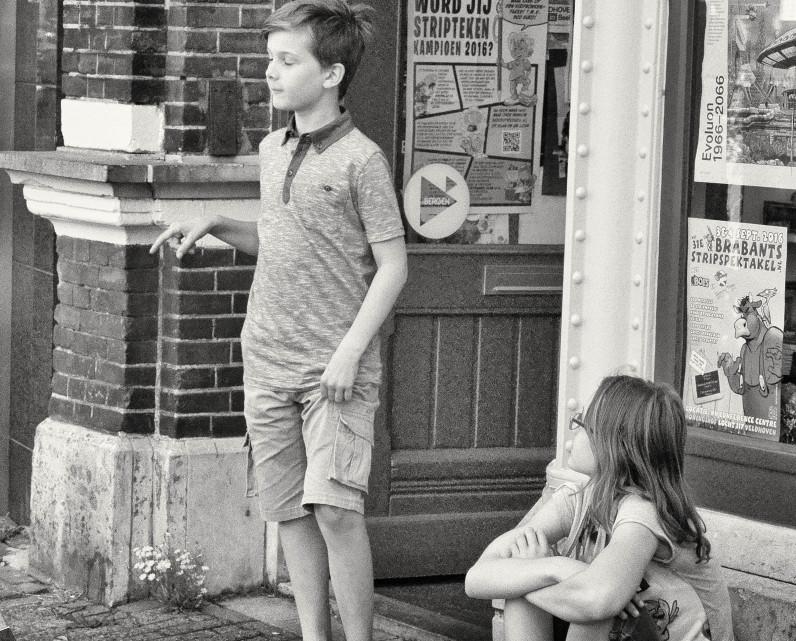 Twee kinderen op straat, waarvan een kind George die zijn taststok vastheeft nadoet.