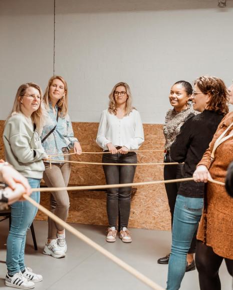 Een groep bezoekers die allemaal een deel van hetzelfde touw vasthebben. Ze communiceren met elkaar om uit de knoop te komen.