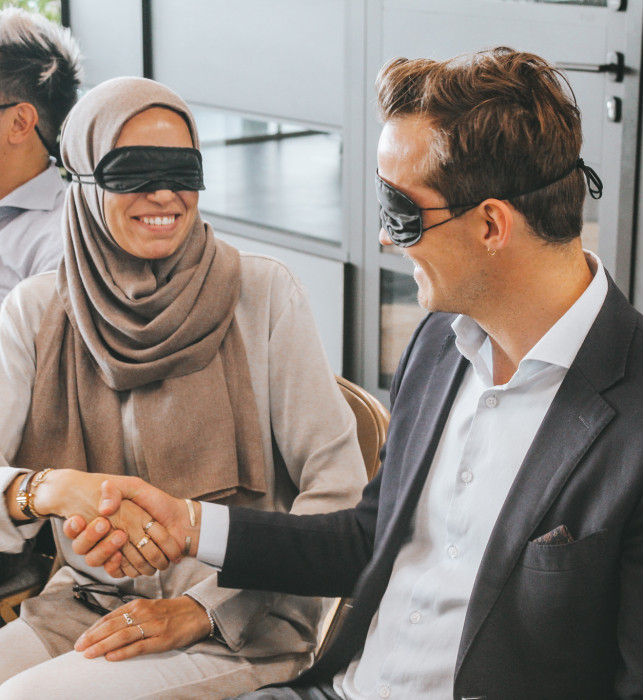 Twee bezoekers zijn geblinddoekt en geven elkaar een hand.