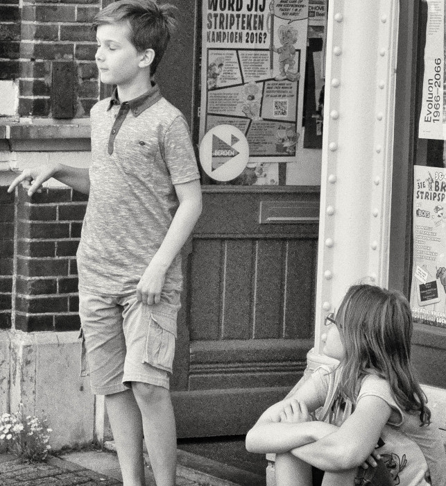 Twee kinderen op straat, waarvan een kind George die zijn taststok vastheeft nadoet.